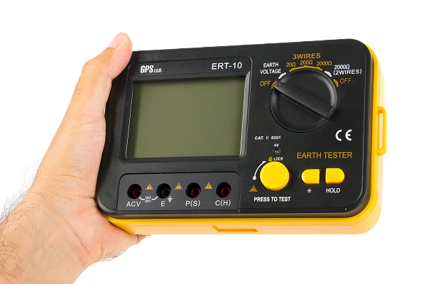 GPS LTD ERT-10 earth resistance tester held in the hand, showing the range dial, backlit display and four input jacks